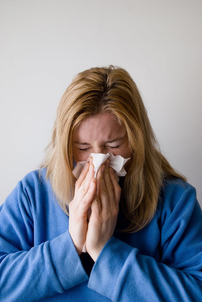 The Art of Drawing Readers In: Your attractive post title goes here A woman in a blue robe is sneezing into a tissue, illustrating symptoms of a cold or flu indoors.