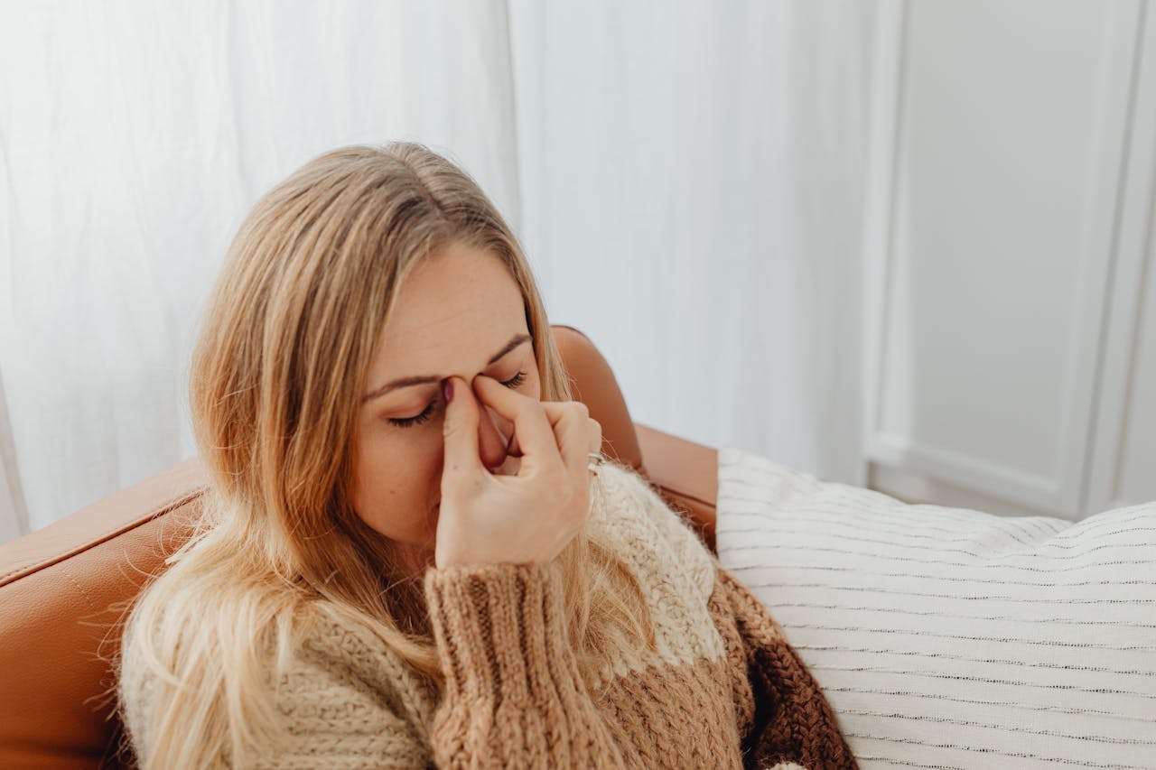 Crafting Captivating Headlines: Your awesome post title goes here A woman sitting on a couch with eyes closed, holding her nose in apparent sinus pain.